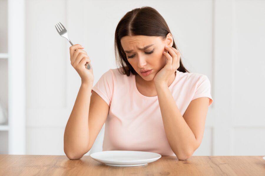 a dissatisfied woman with an empty plate in front of her because of Intermittent Fasting